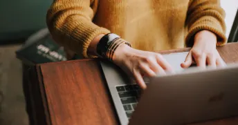 Person iklädd en lejongul stickad tröja som knappar på en laptop.