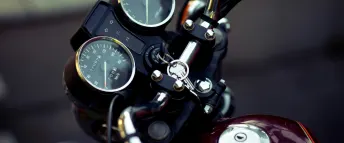 Närbild på en motorcykels styre med hastighetsmätare och nyckel.