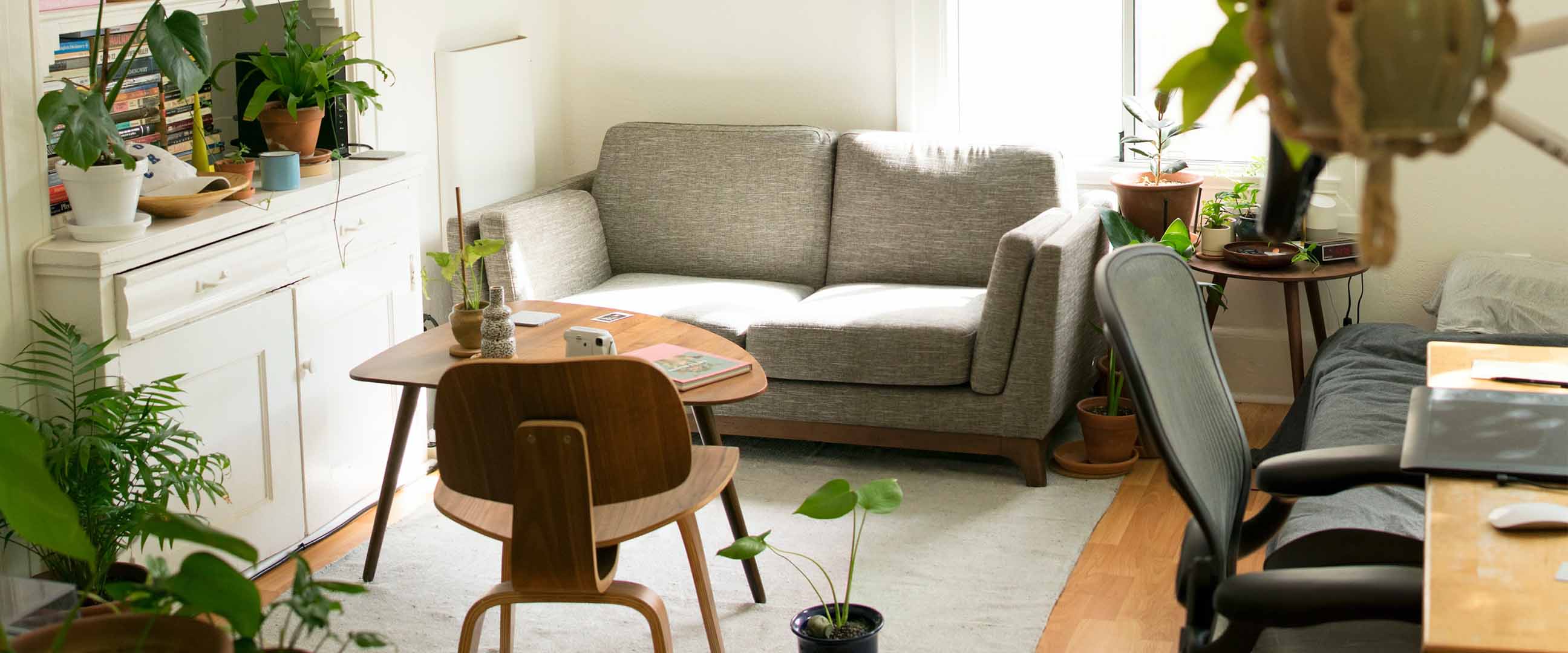 Vardagsrum med vita väggar, grå soffa, skrivbordsstol och soffbordet Lövet från IKEA.