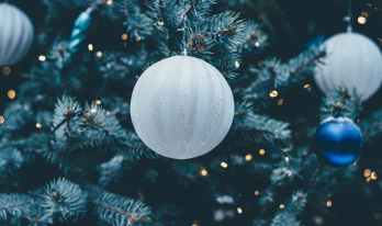 Närbild på en vit julgranskula hängades i en julgran med ljusslingor och andra julgranskulor i blått och vitt i bakgrunden