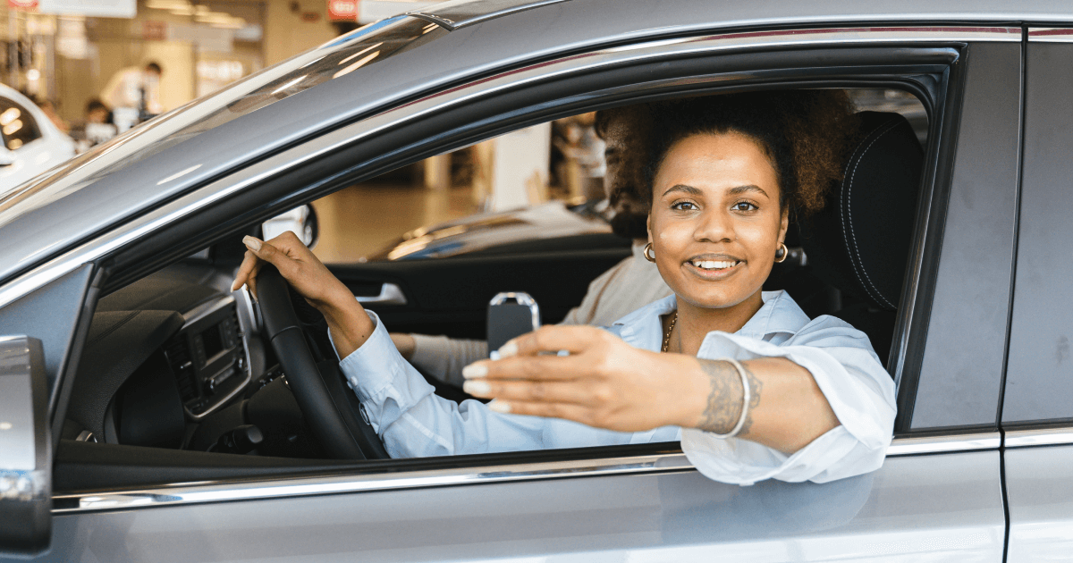Kvinna som ler sitter i förarsätet i en bil och sträcker ut bilnycklarna genom fönsterrutan.