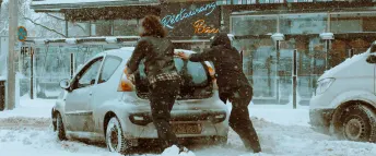 Två personer som försöker få loss en silvrig bil som har kört fast i snön på Götgatan, Södermalm i Stockholm