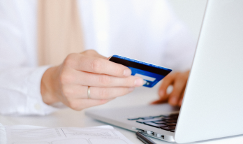Hand som håller i ett blått kreditkort framför en laptop. 