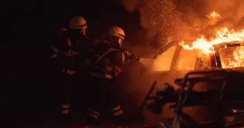 Två brandmän bekämpar en bilbrand.