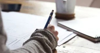 Närbild på hand på en person som planerar och skriver ner anteckningar med en blå penna.