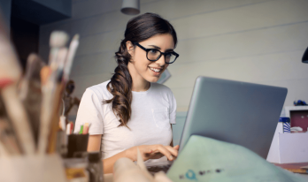 Leende kvinna med glasögon tittar på datorskärm