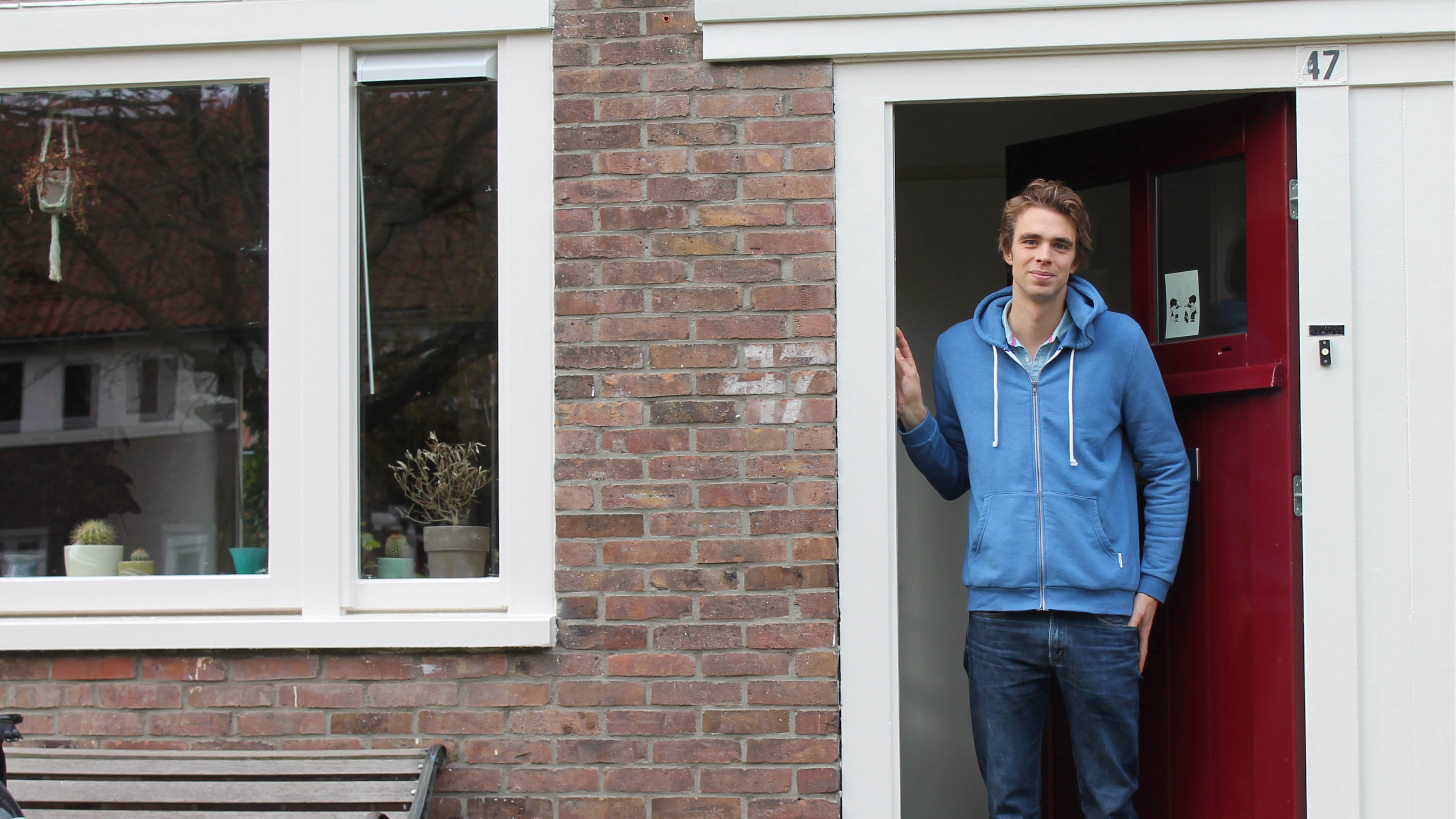 Man in blauw vest staat in deurpost met rode deur