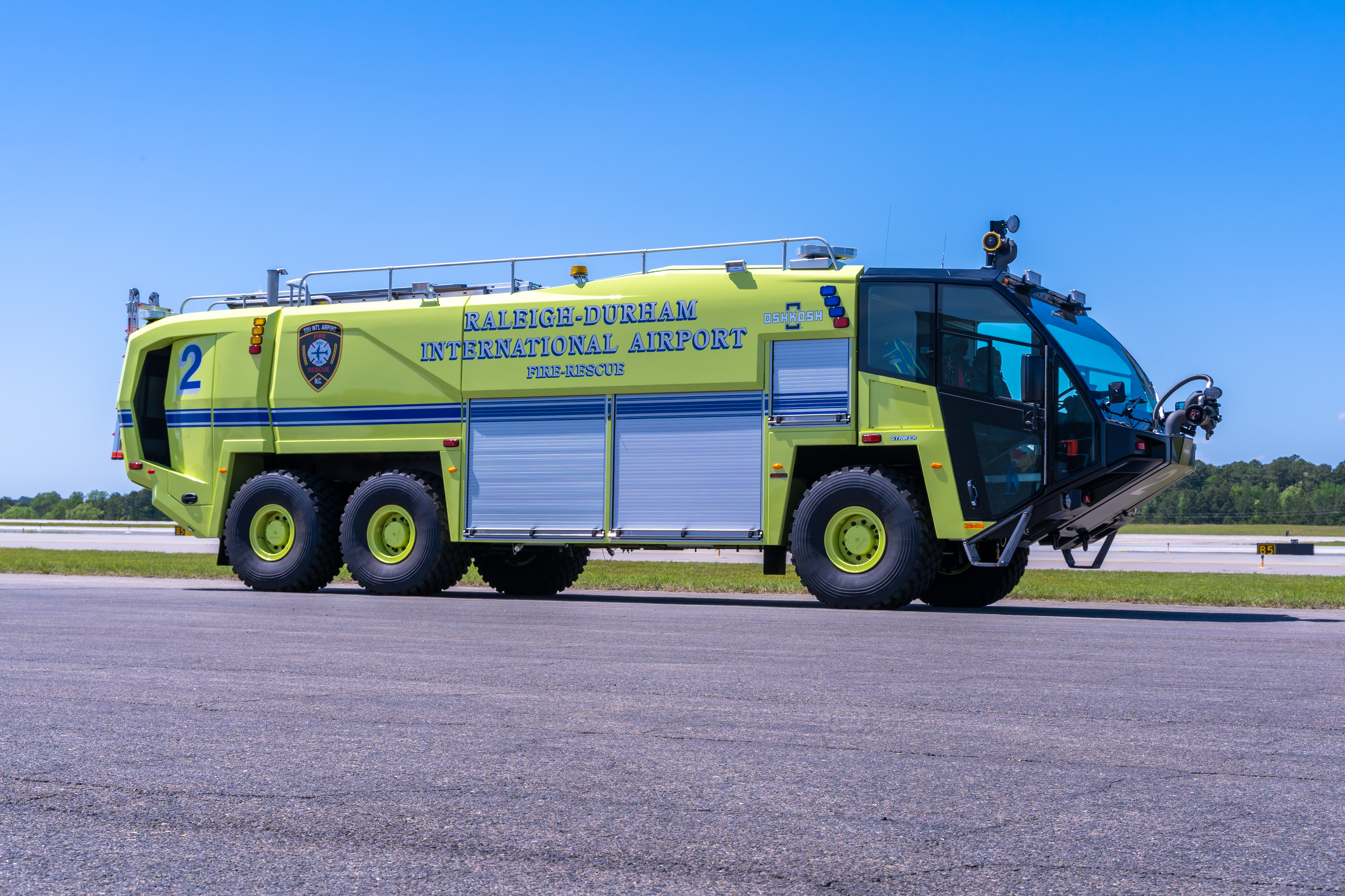 Bright yellow-green airport fire rescue truck labeled Raleigh-Durham International Airport parked on tarmac under clear blue sky.