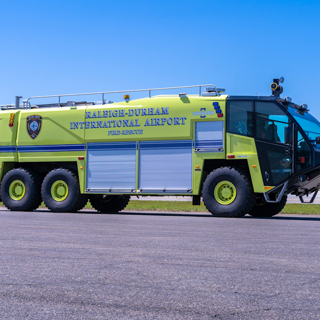 Bright yellow-green airport fire rescue truck labeled Raleigh-Durham International Airport parked on tarmac under clear blue sky.