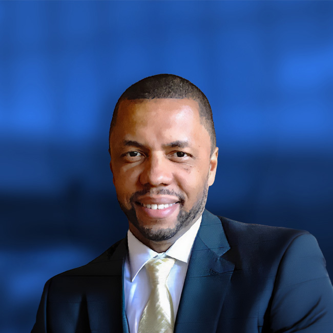 Professional headshot of a smiling man in a dark suit with gold tie against a blue background