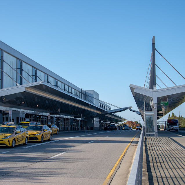 Modern airport terminal with yellow taxis lined up outside under a clear blue sky and distinctive angular architecture.
