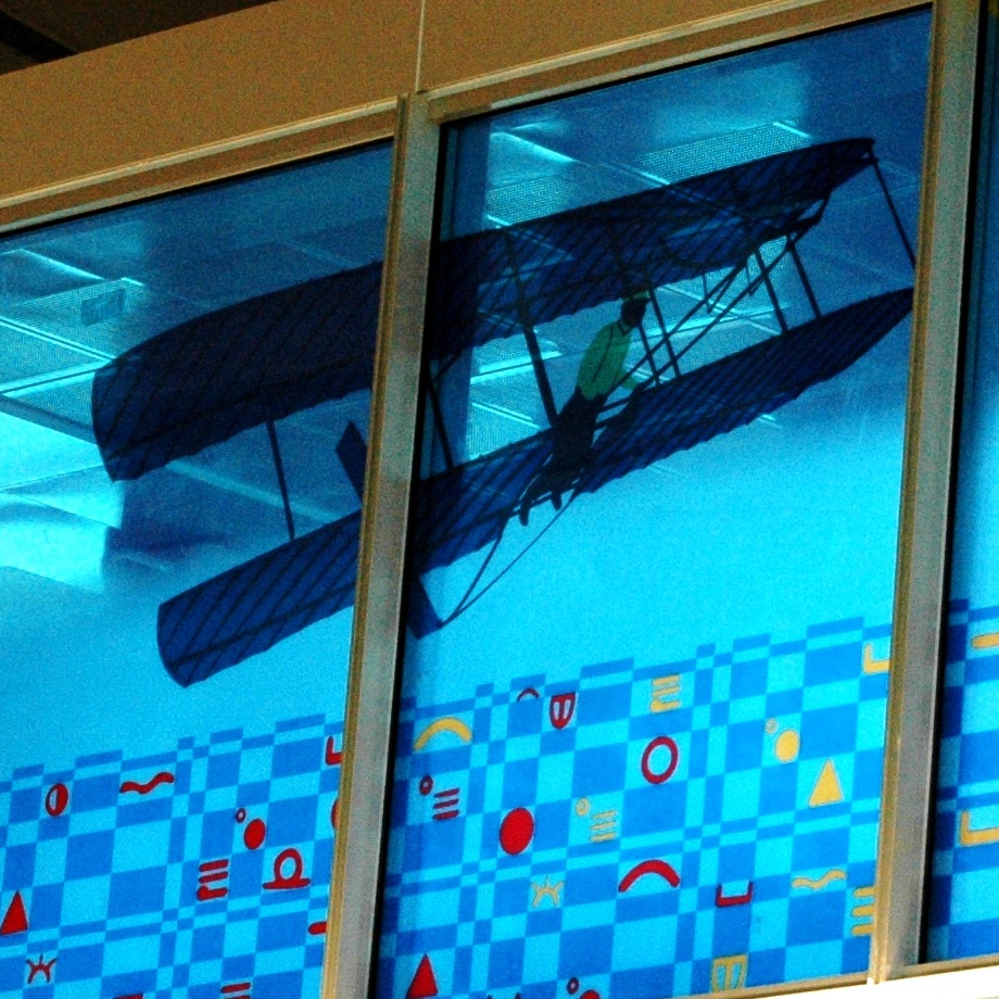 Blue glass windows with vintage biplane silhouettes and yellow decorative swirls in an airport terminal interior.
