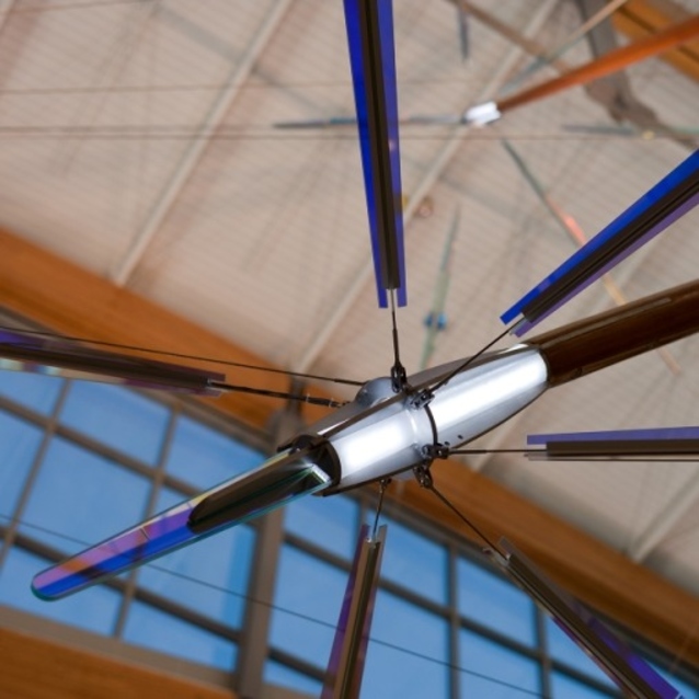 Close-up of a metallic ceiling fixture with colorful glass rods radiating outward against a beige ceiling and windows.