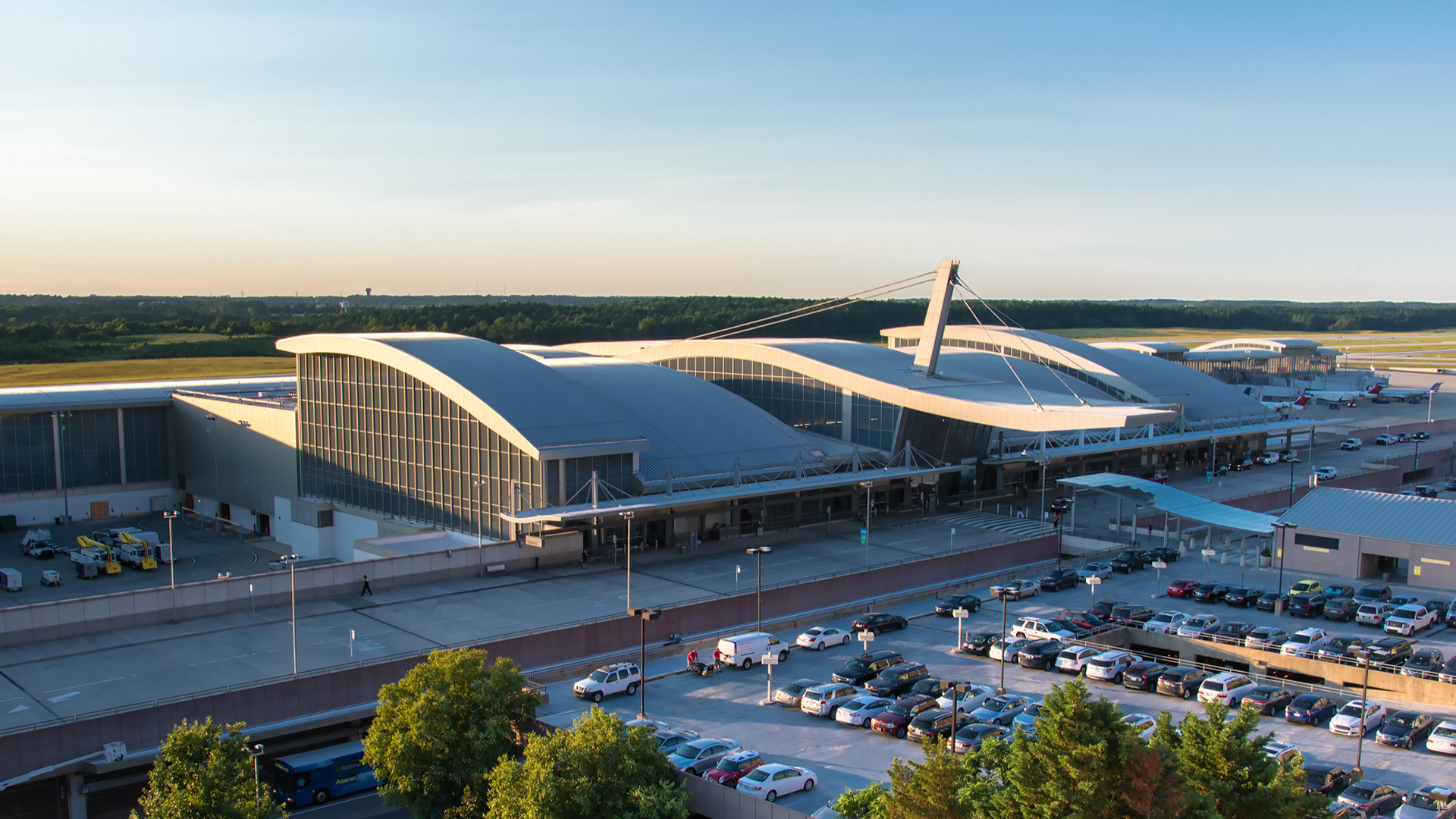 RDU's Terminal 2, with distinctive angular roof and cable-stayed tower, vehicles in the departure area, against a clear blue sky.