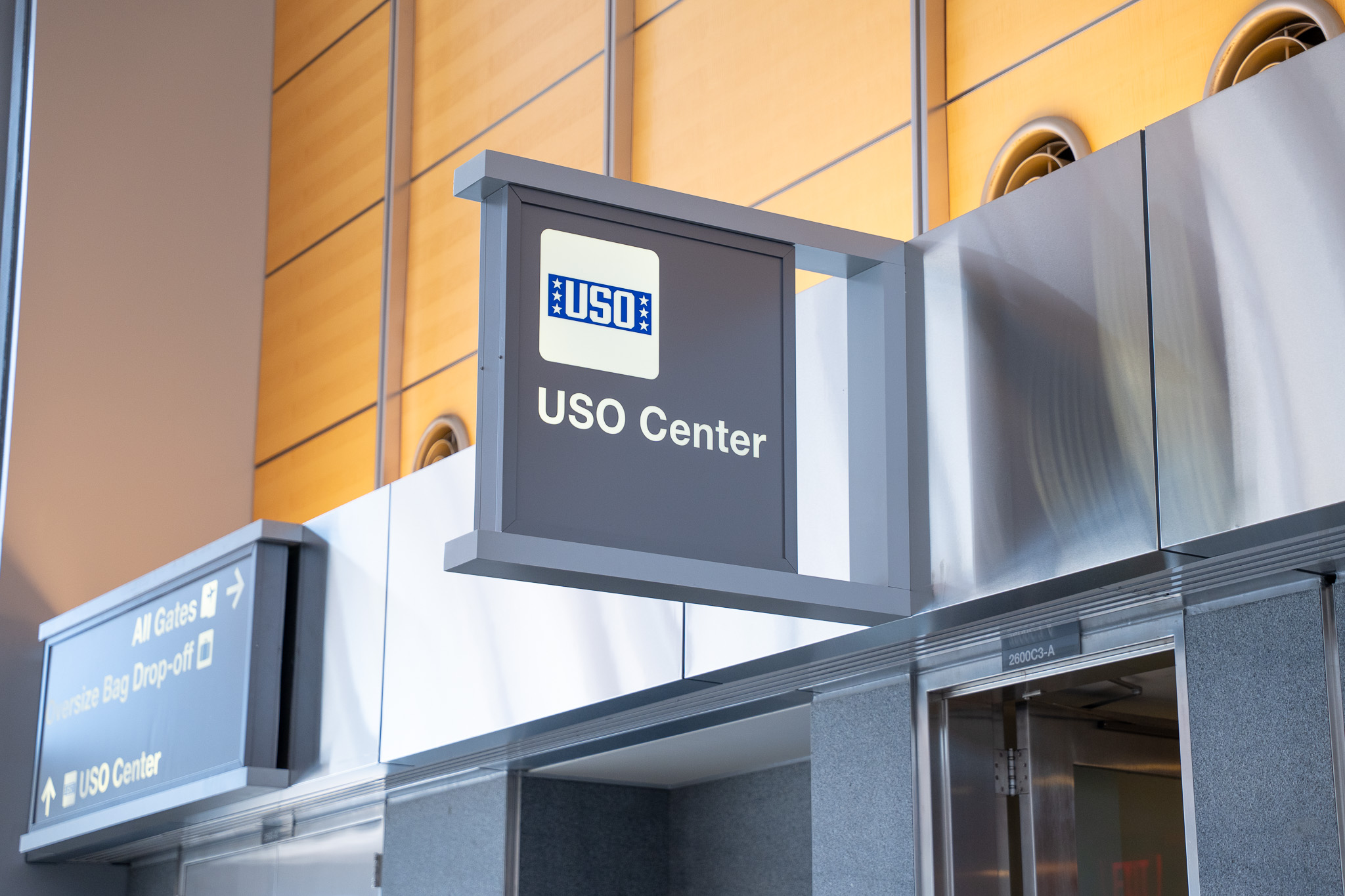 USO Center sign with blue and white logo mounted on gray frame against yellow wall in airport terminal.