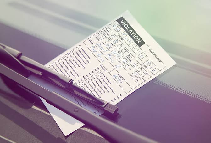 A parking violation ticket placed under a car's windshield wiper on the front windshield of a vehicle.