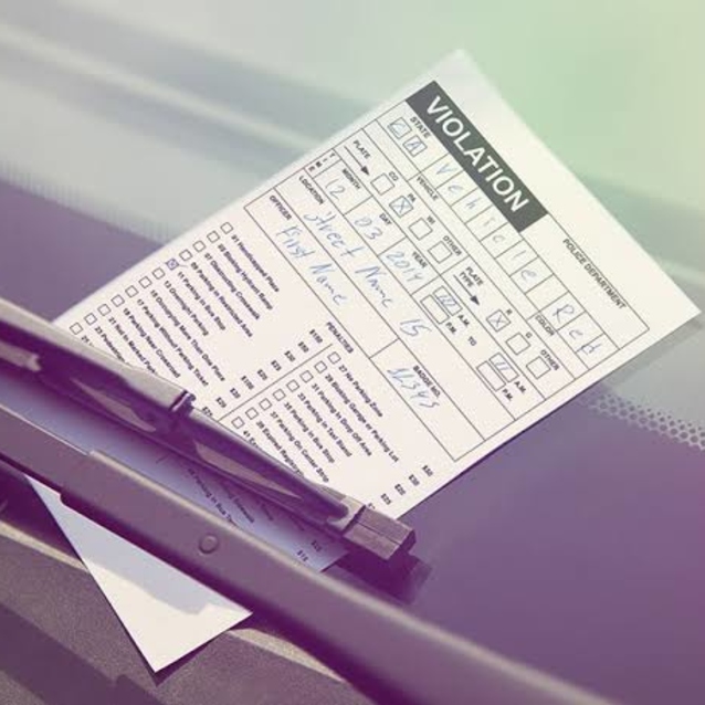 A parking violation ticket placed under a car's windshield wiper on the front windshield of a vehicle.