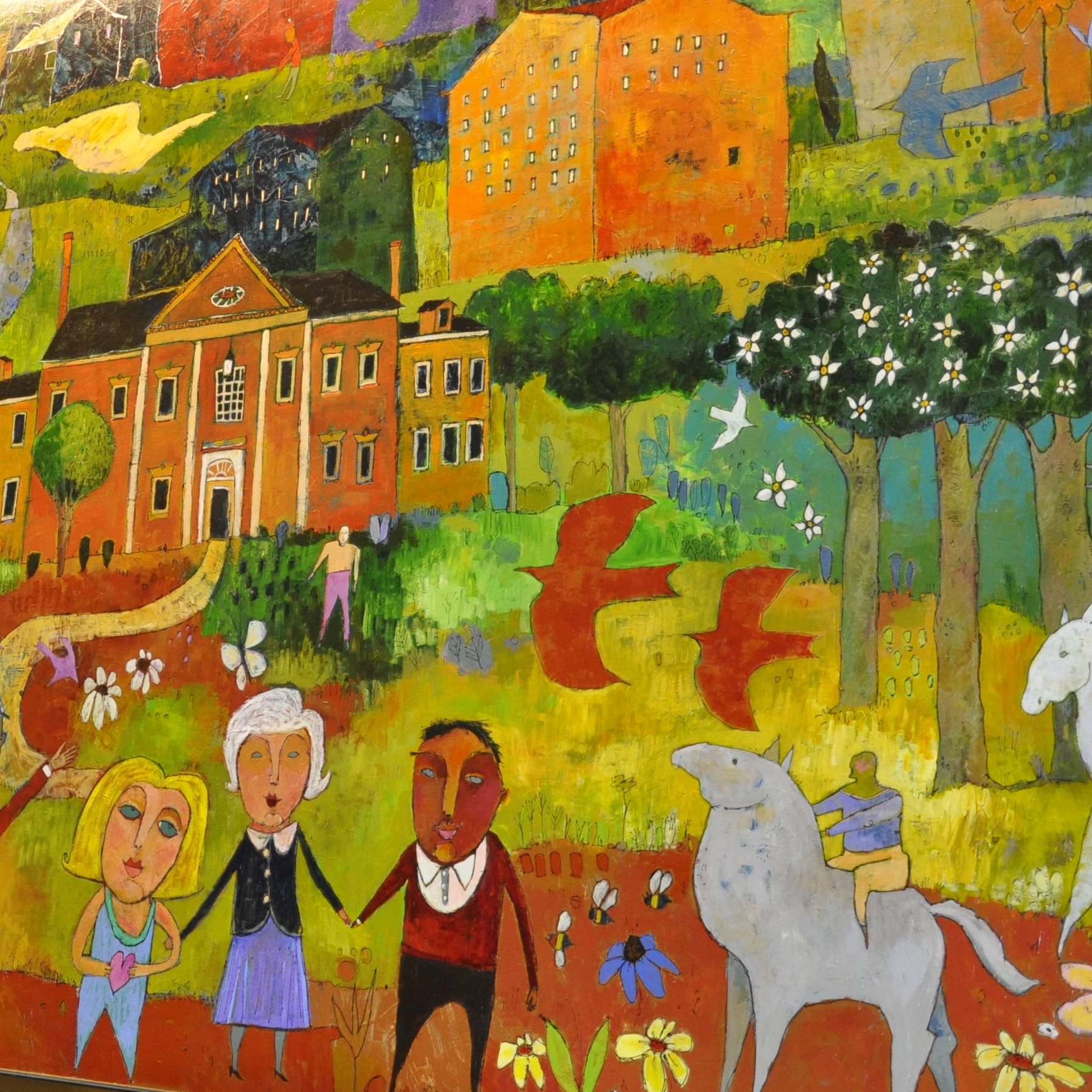Colorful mural depicting diverse people, buildings, animals, and nature in vibrant oranges, greens, and yellows on an indoor wall.