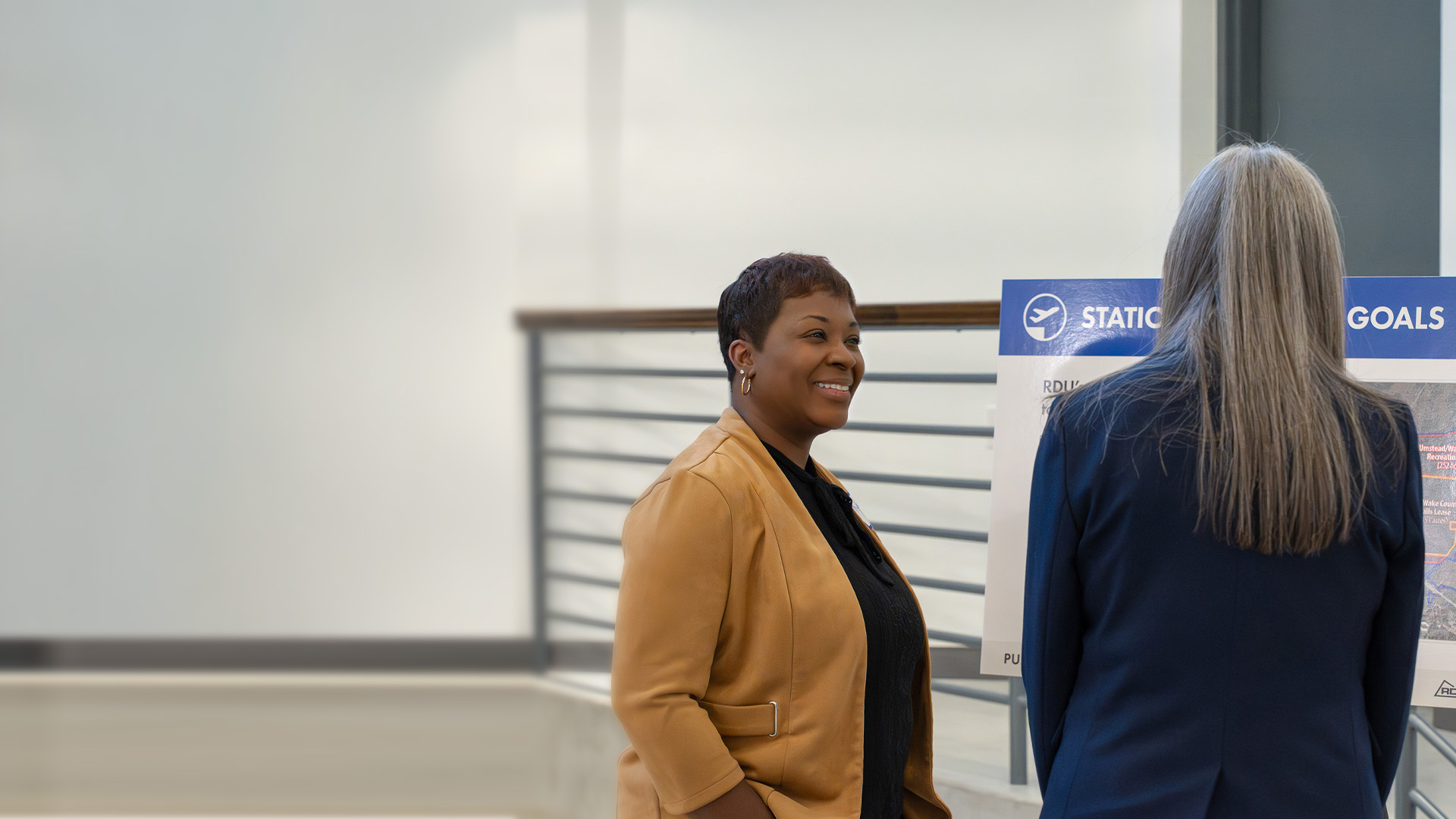 An RDU employee engaging with a member of the public. The employee is wearing a brown jacket and smiling.