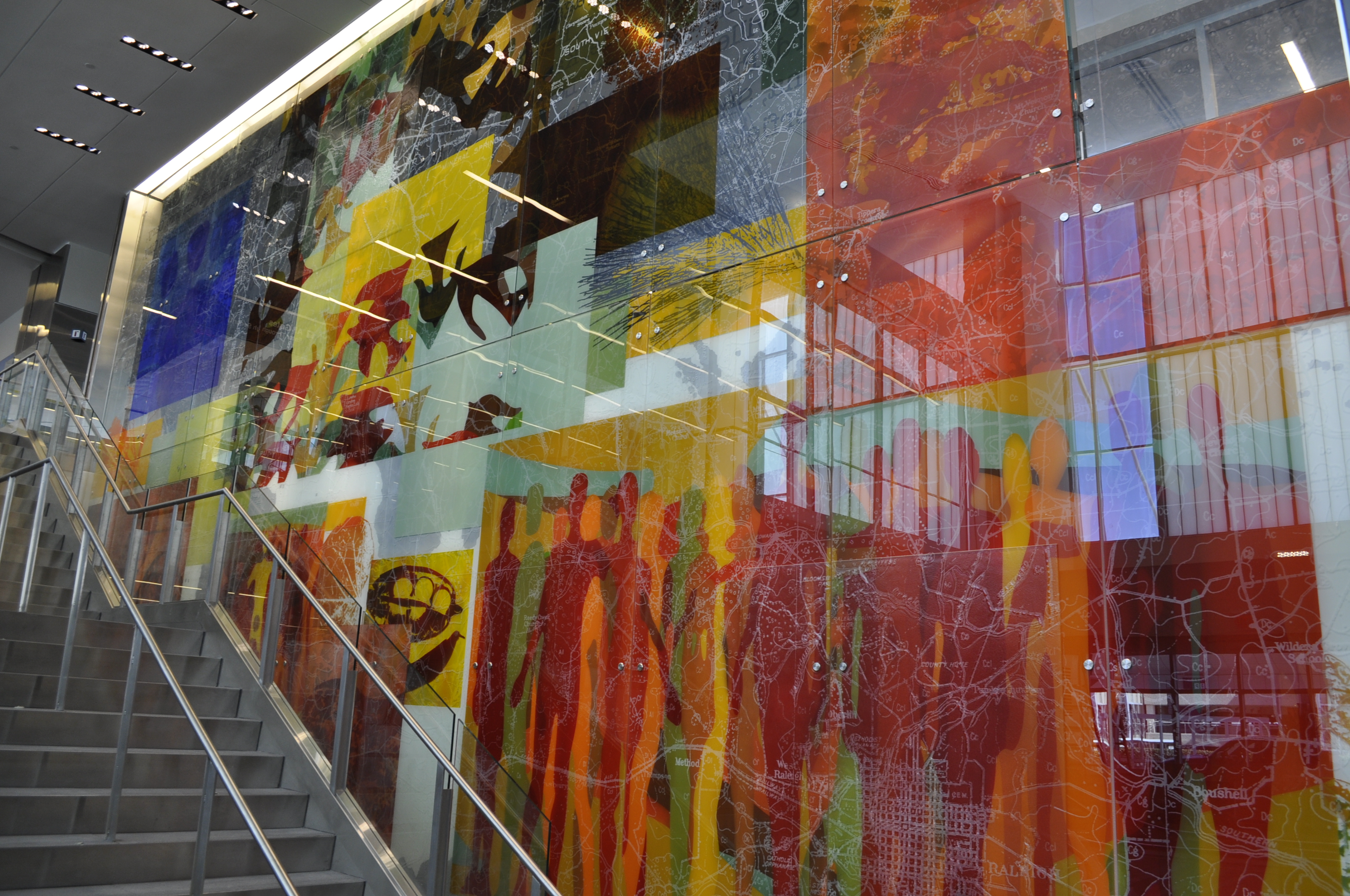 Large colorful abstract mural with overlapping geometric shapes and patterns in blue, yellow, red, and orange beside a staircase.