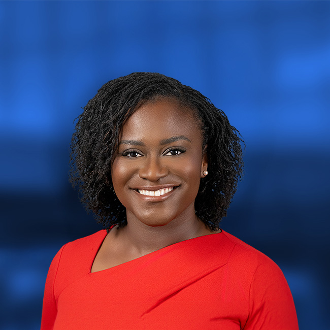 Professional headshot of a smiling woman with shoulder-length black hair wearing a bright red top against a blue background.