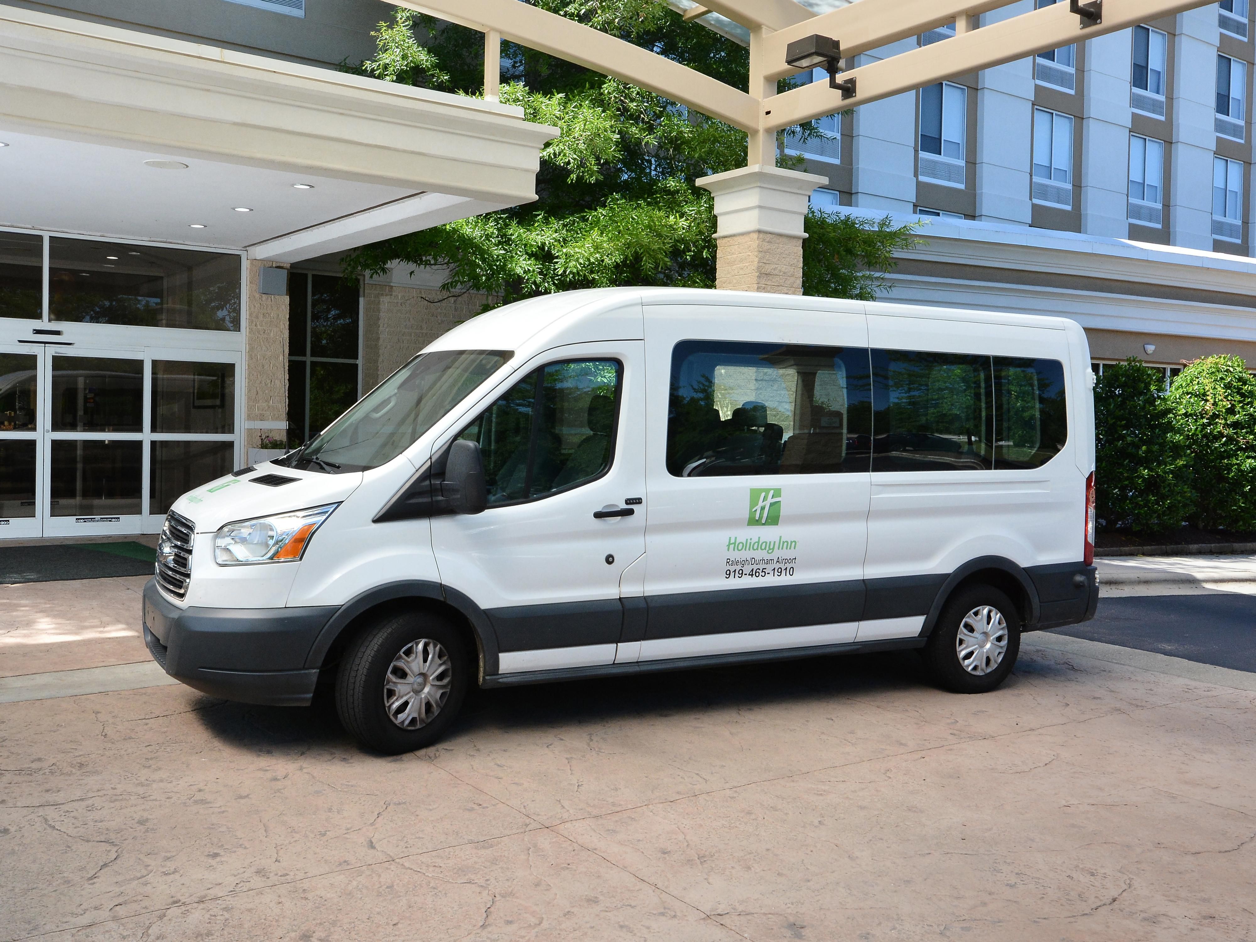 White Holiday Inn shuttle van parked under hotel entrance canopy with modern building in background.