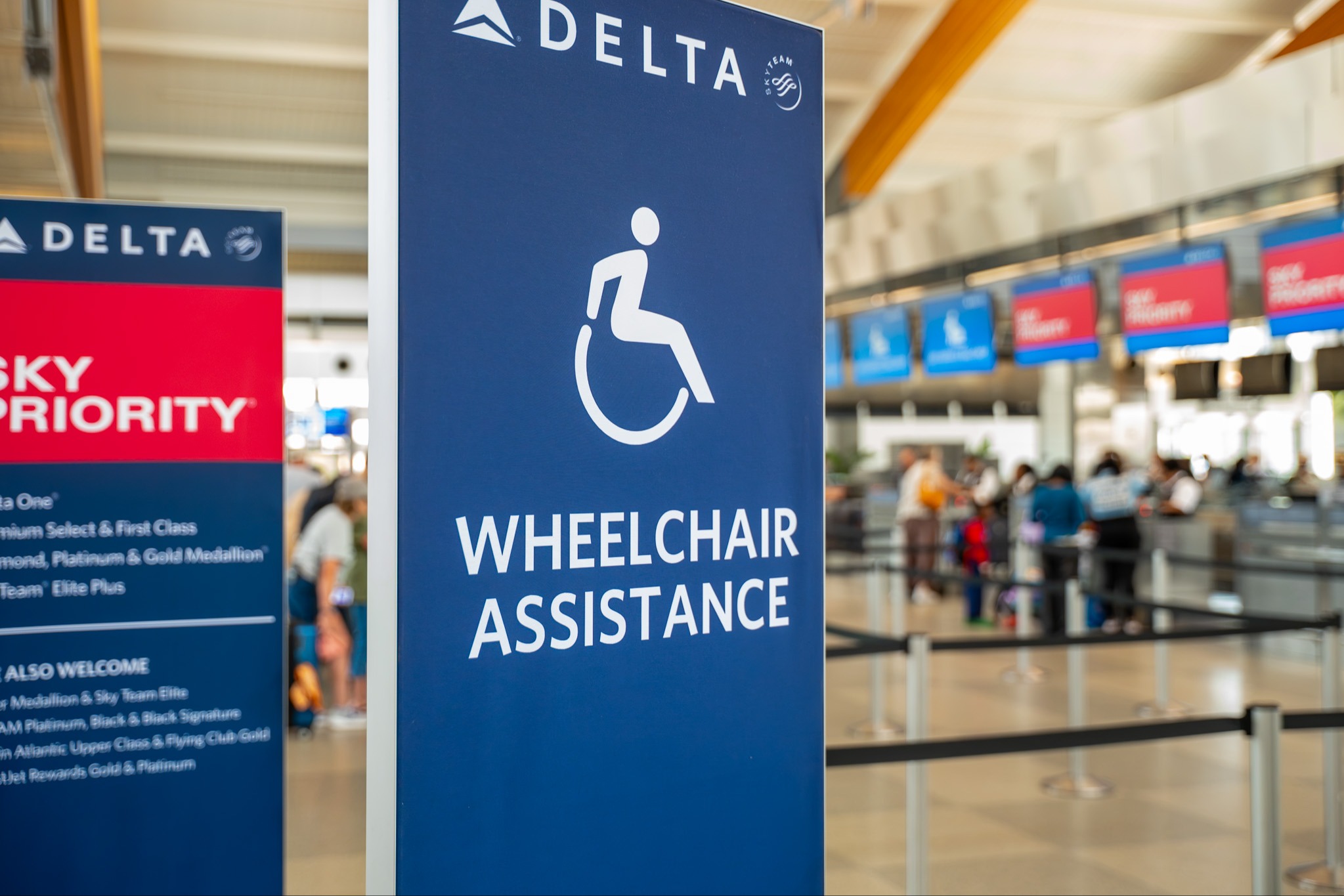 Delta wheelchair assistance sign with accessibility icon in airport terminal with travelers in background.
