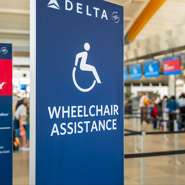 Delta wheelchair assistance sign with accessibility icon in airport terminal with travelers in background.