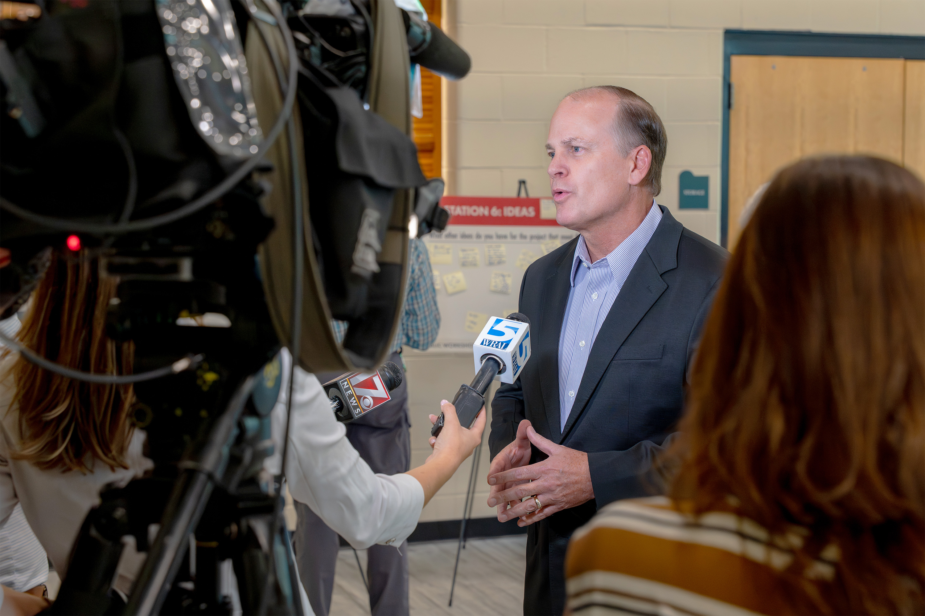A person is speaking to reporters and camera crews in a room with beige walls. Several microphones, including one with the logo "KWTX," are directed toward the speaker.
