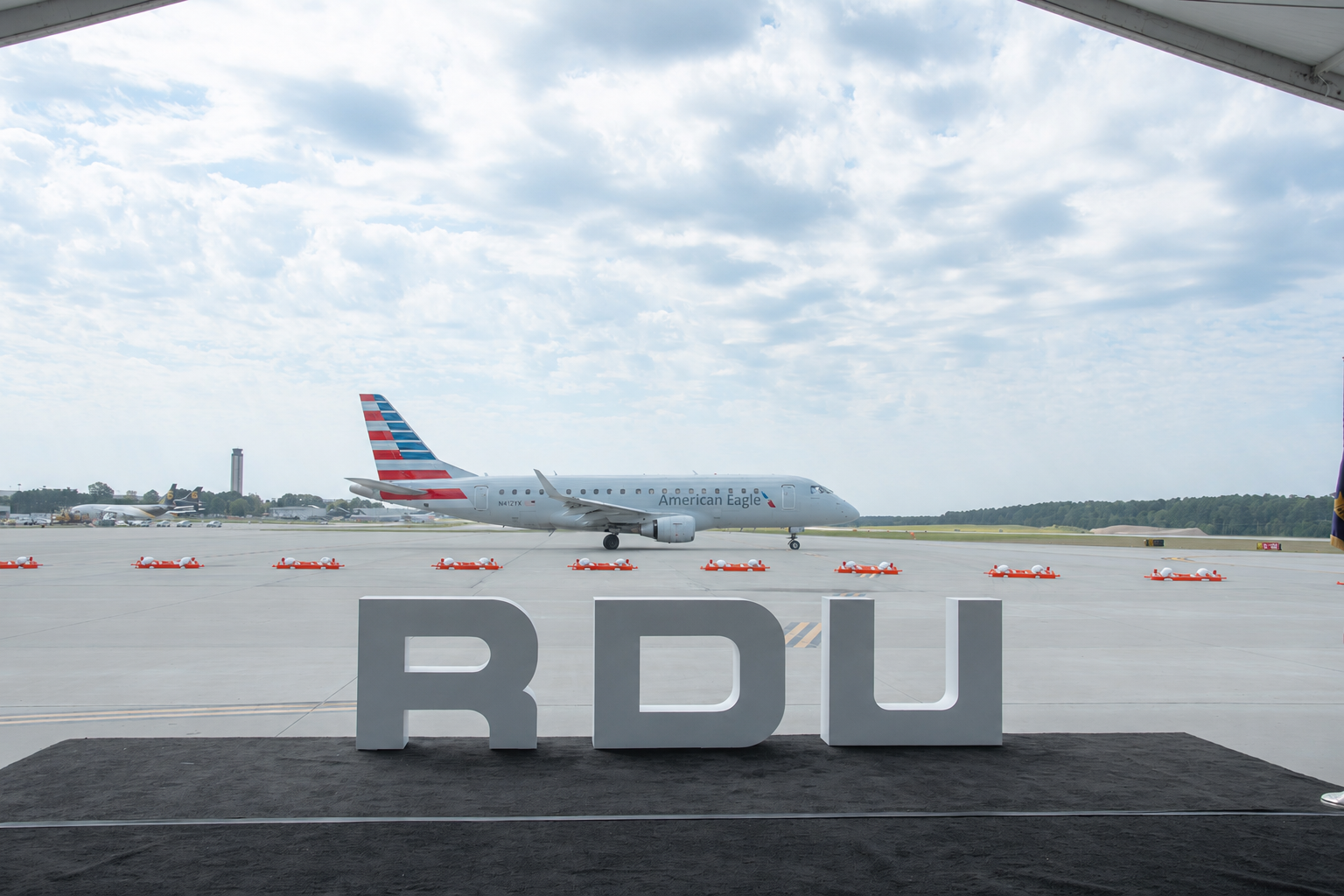 American Eagle aircraft taxiing on runway with large RDU airport sign in foreground under cloudy sky.