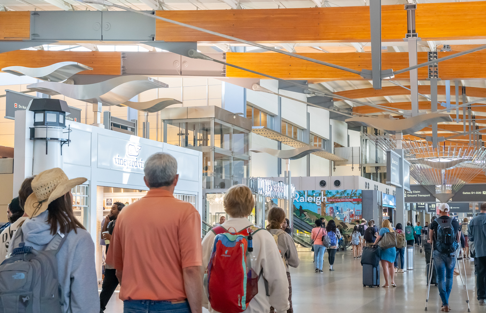 Travelers walking through Raleigh-Durham International Airport Terminal 2 with wooden ceiling beams and white sculptural elements overhead.