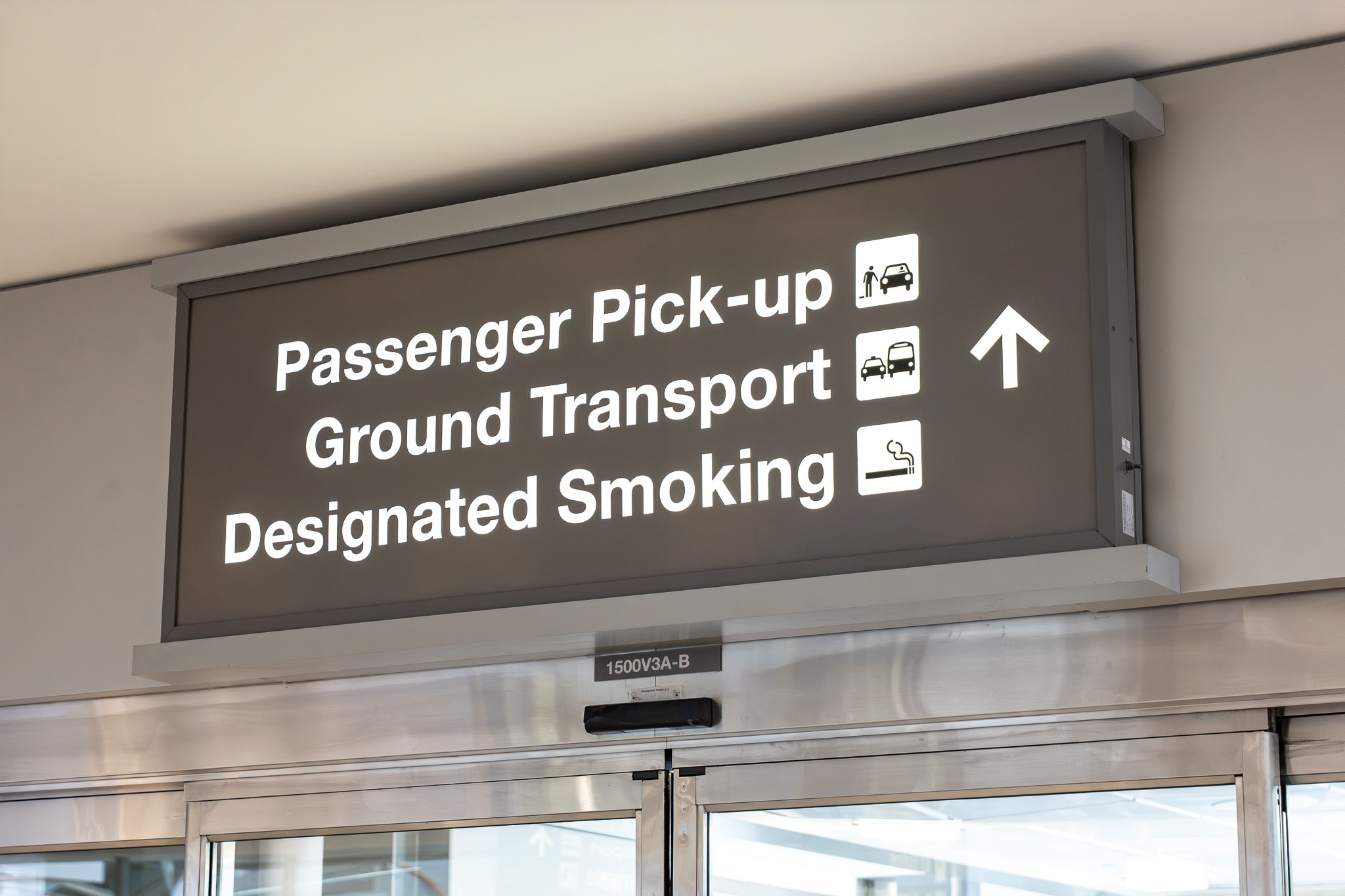 Airport directional sign showing Passenger Pick-up, Ground Transport, and Designated Smoking areas with upward arrow.