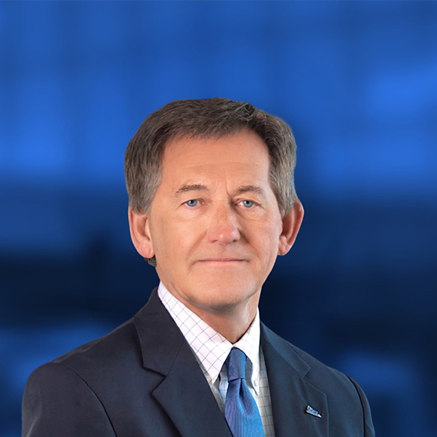 Professional headshot of a man in a dark suit and blue tie against a blue gradient background, looking directly at camera.
