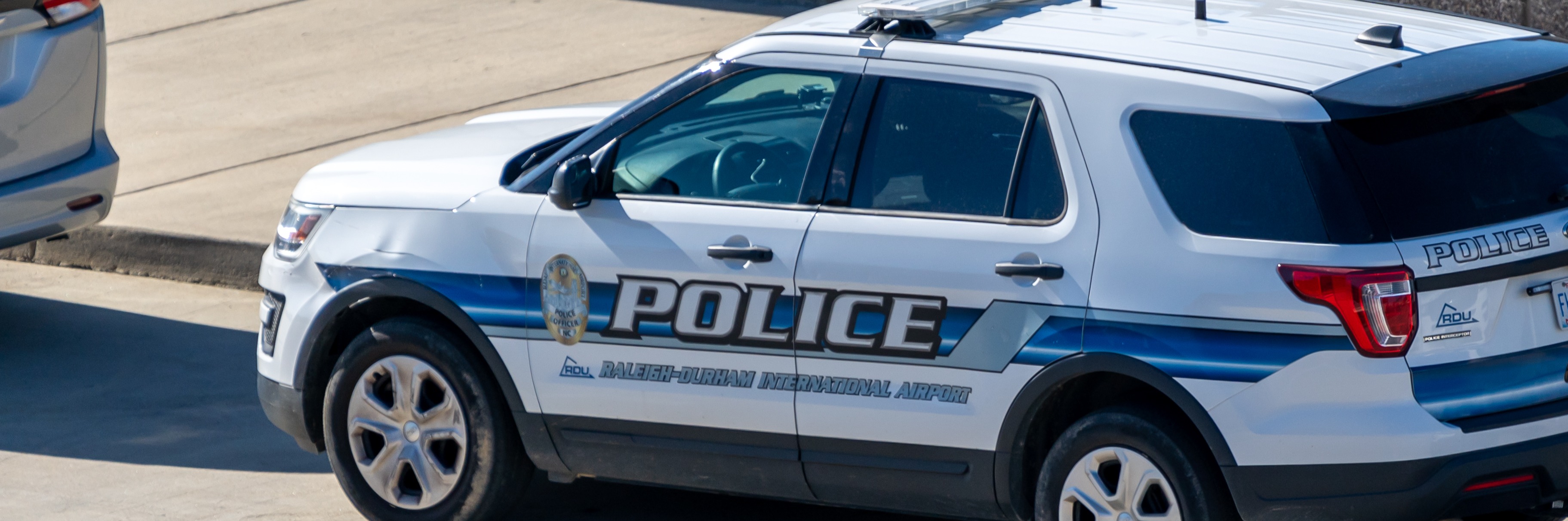 White police SUV with Raleigh-Durham International Airport markings parked on pavement near a concrete wall.