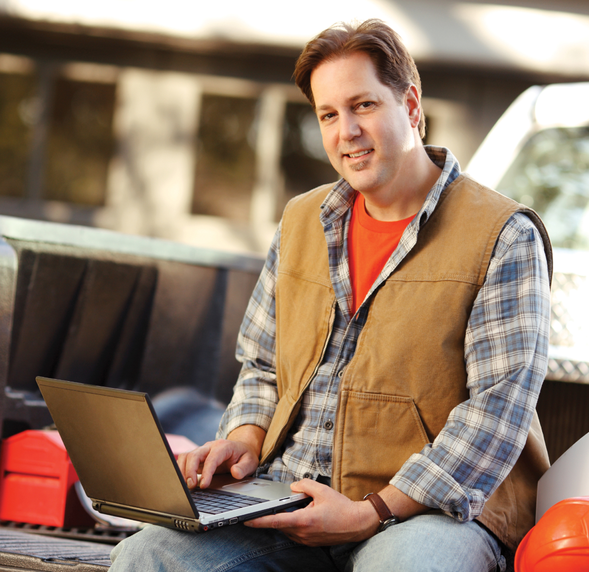 A business owner sitting on the back of their truck while using a laptop computer