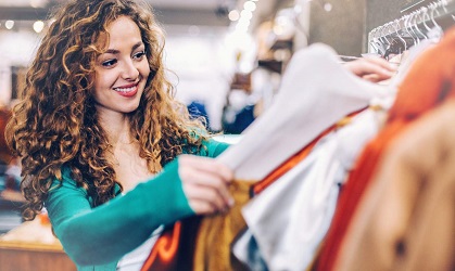 Une femme souriante regarde des vêtements sur un portant dans un magasin.