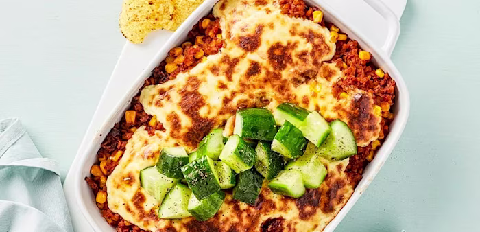 En form med tacogratäng med gurka på toppen och nachochips bredvid