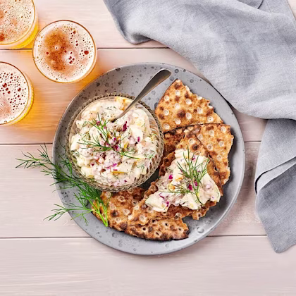 Kryddig sillröra på knäckebröd på tallrik med dill och en grå duk.