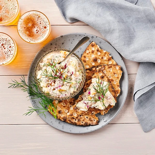 Kryddig sillröra på knäckebröd på tallrik med dill och en grå duk.