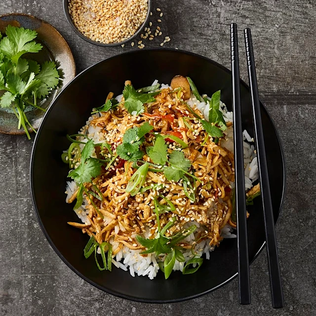 Djup tallrik med ris och wok. Toppad med sesamfrön och korriander.