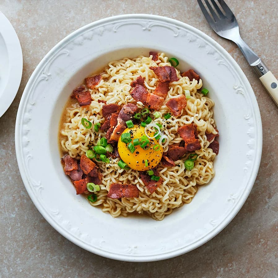 En djup tallrik med nudlar, bitar av kött och en äggula. Toppad med hackad salladslök. 