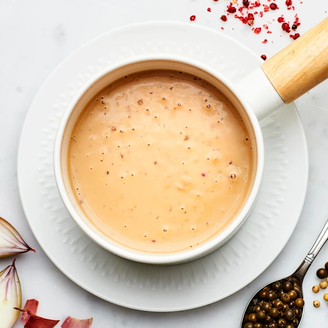 En vit skål med pepparsås, står på en vit tallrik. Peppar och scarlottenlök ligger bredvid tallriken som dekoration.