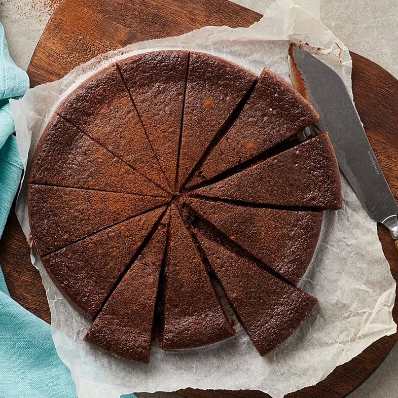 En uppskuren kladdkaka i perfekta tårtbitar. Kakan ligger på bakplåtspapper med en kniv intill sig. 