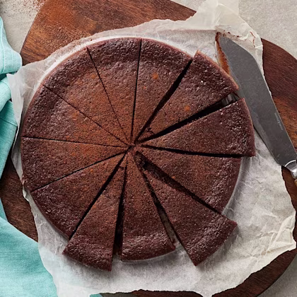 En uppskuren kladdkaka i perfekta tårtbitar. Kakan ligger på bakplåtspapper med en kniv intill sig.