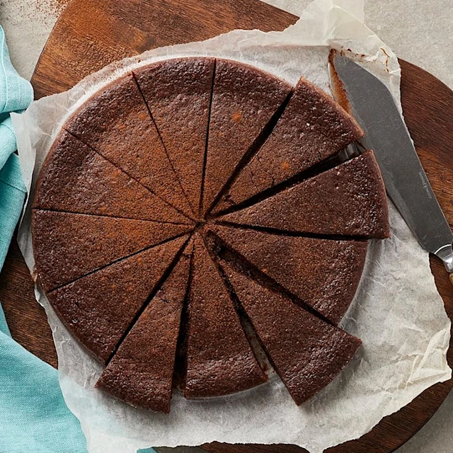 En uppskuren kladdkaka i perfekta tårtbitar. Kakan ligger på bakplåtspapper med en kniv intill sig.