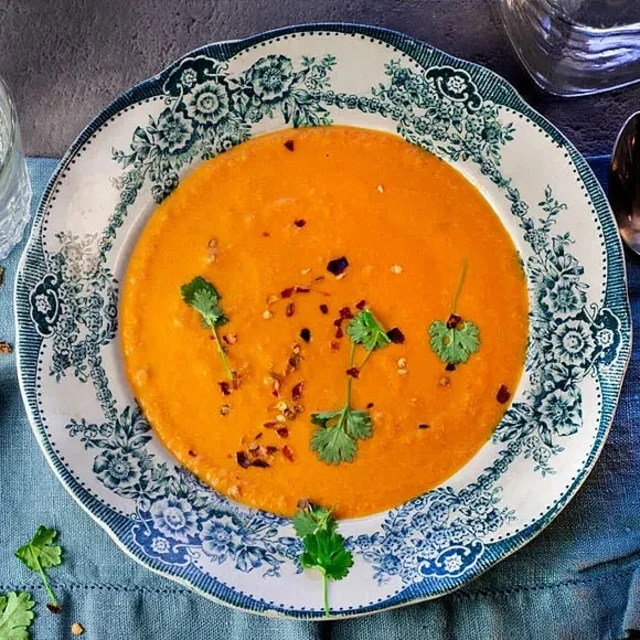 En antik djup talrik med blått kringlande mönster, fylld med en krämig orange morotssoppa som är toppad med färsk korriander.