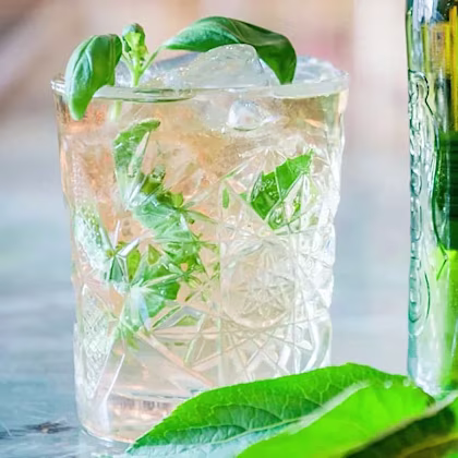 Drink med is och gröna örter i mönstrat glas, bredvid gröna blad och flaska.