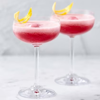Rosa drinkar med skum i cocktailglas, dekorerade med citronskal på marmorbord.