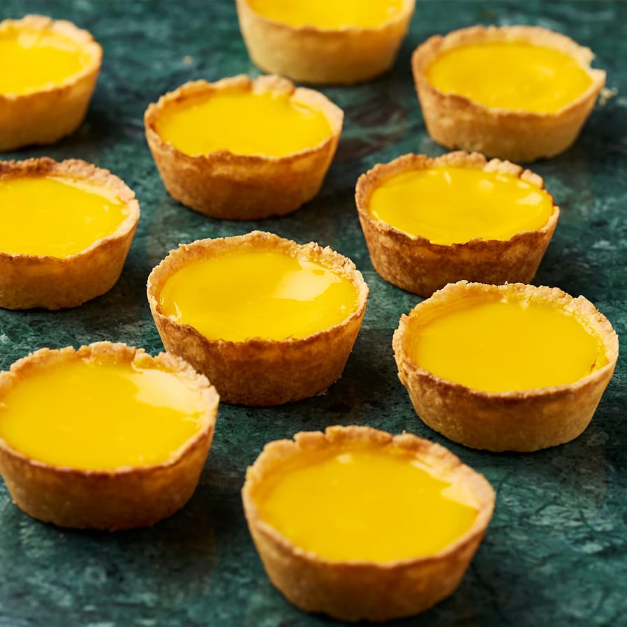 Små pajskalen med gyllene fyllning är placerade på en grön yta. De ser läckra och inbjudande ut.