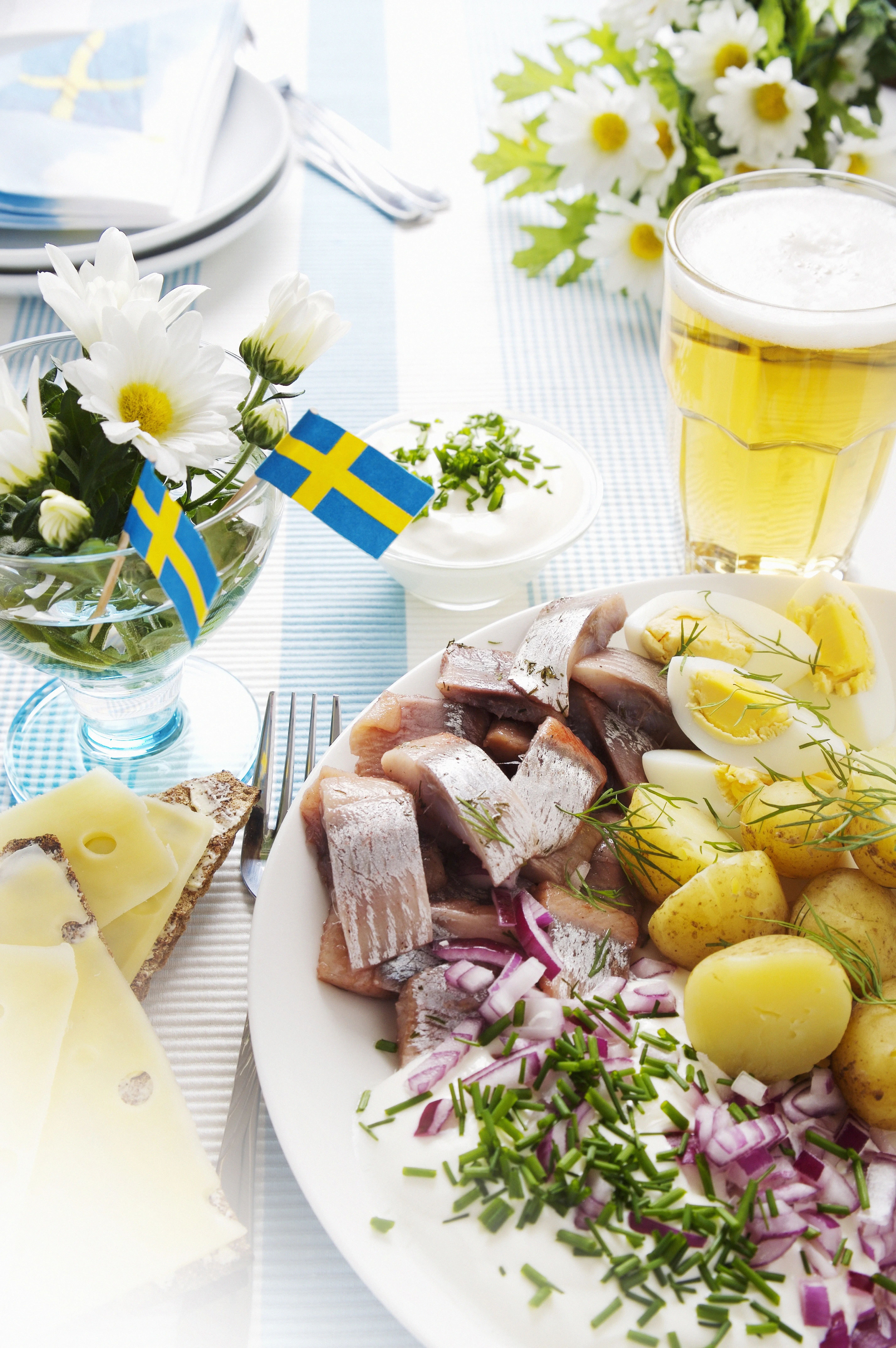 Tallrik med sill, kokt potatis, ägg och hackad lök och svenska flaggor.